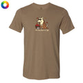 A heather brown short-sleeve t-shirt with a cartoon graphic of a dog wearing a plaid blanket and holding a basket of red apples, with the text 'the dog days of fall' printed below. A small circular color wheel icon is in the top-left corner.
