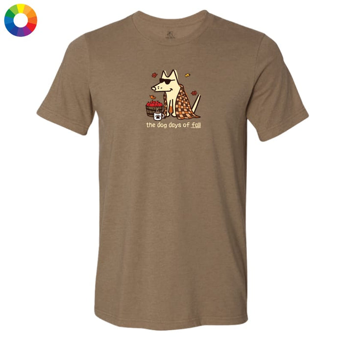 A heather brown short-sleeve t-shirt with a cartoon graphic of a dog wearing a plaid blanket and holding a basket of red apples, with the text 'the dog days of fall' printed below. A small circular color wheel icon is in the top-left corner.