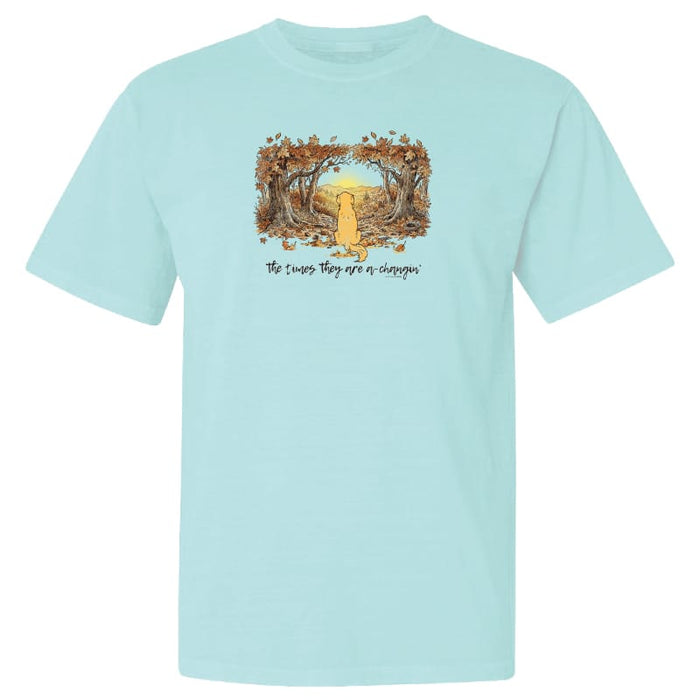 A light aqua blue short-sleeve crewneck t-shirt featuring a central graphic of a yellow dog sitting in a forest of falling leaves with the text 'The Cactus They Eat or Choke' printed below.