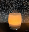 to the moon light grey and white, hand-blown glass votive candle holder on dark surface with a starry night background.