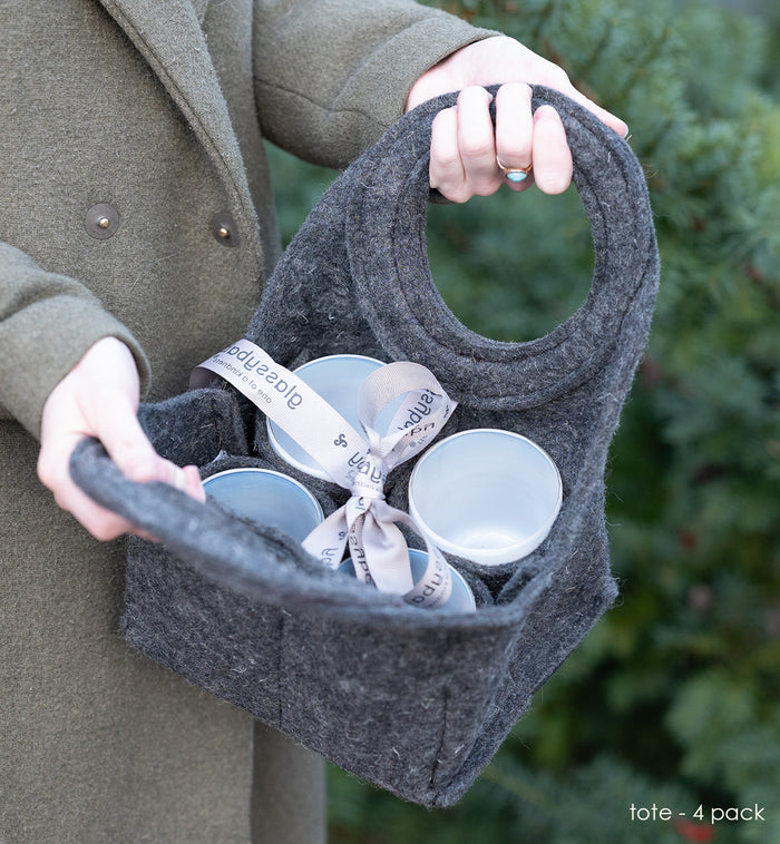 felt tote with four hand-blown drinking glasses being carried by woman in trench coat.