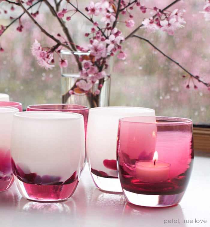 true love, transparent deep raspberry pink, hand-blown glass votive candle holder. Paired with petal on a white table with flowers in background.