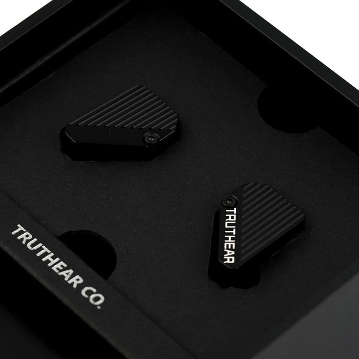 A close-up of two black, angular TRUTHEAR Pure In-Ear Headphones with diagonal grooves rests in a foam insert inside a black box, one marked with TRUTHEAR, showcasing their hybrid 4-driver design and outstanding sound quality.
