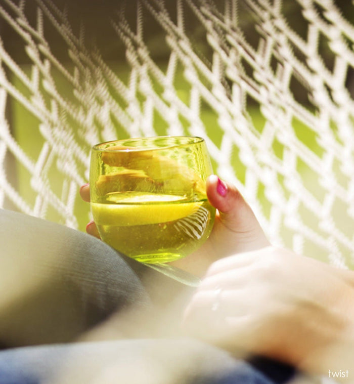 twist drinker, transparent lime green, hand-blown drinking glass being held by a person laying in a hammock.