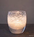 Glass candle holder with wavy design on a dark surface and gray background