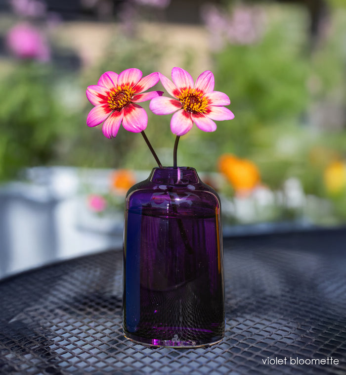 violet bloomette - purple vase with pink flowers on metal table outside.