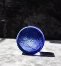 Blue pedestal with 'glassybaby' branding on a white surface with a dark background