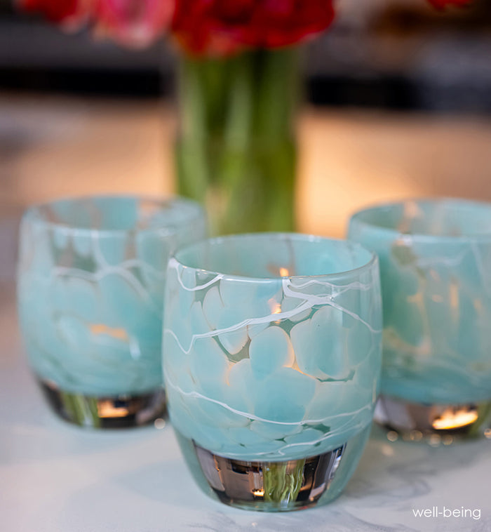 Three turquoise with white marbled pattern glass candle holders with a blurred floral background