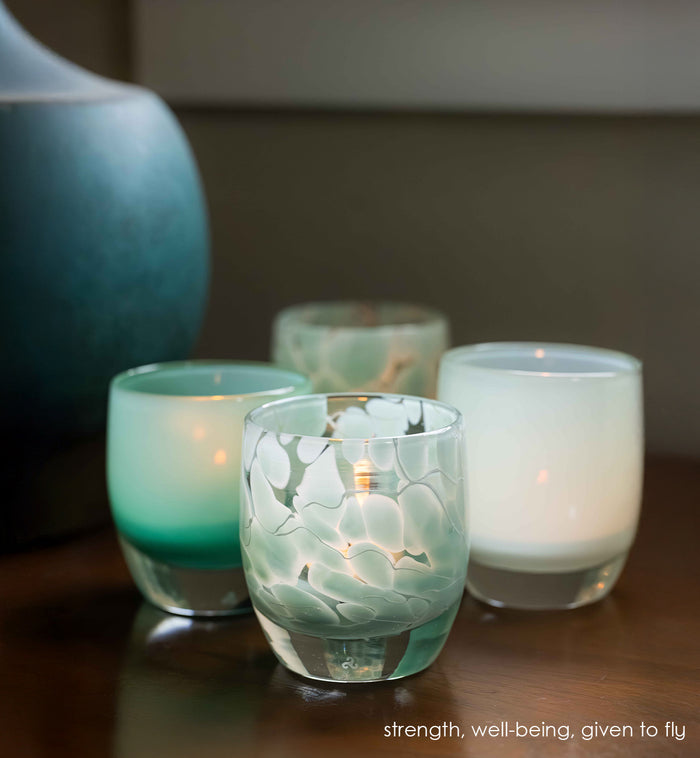 Turquoise with white marbled pattern glass candle holder with green candle holders next to it.
