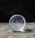 white transparent glass pedestal with 'glassybaby' branding on a gray surface with a dark background