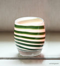 green stripes on a white base create beautiful wintergreen, a hand-blown glass votive candle holder with a lit tealight on a white table